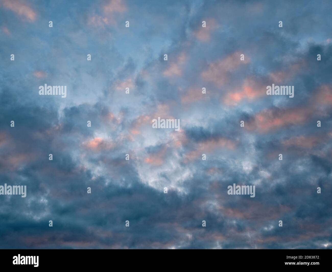 Abstract image of pink and orange clouds against a blue sky at sunset. Stock Photo
