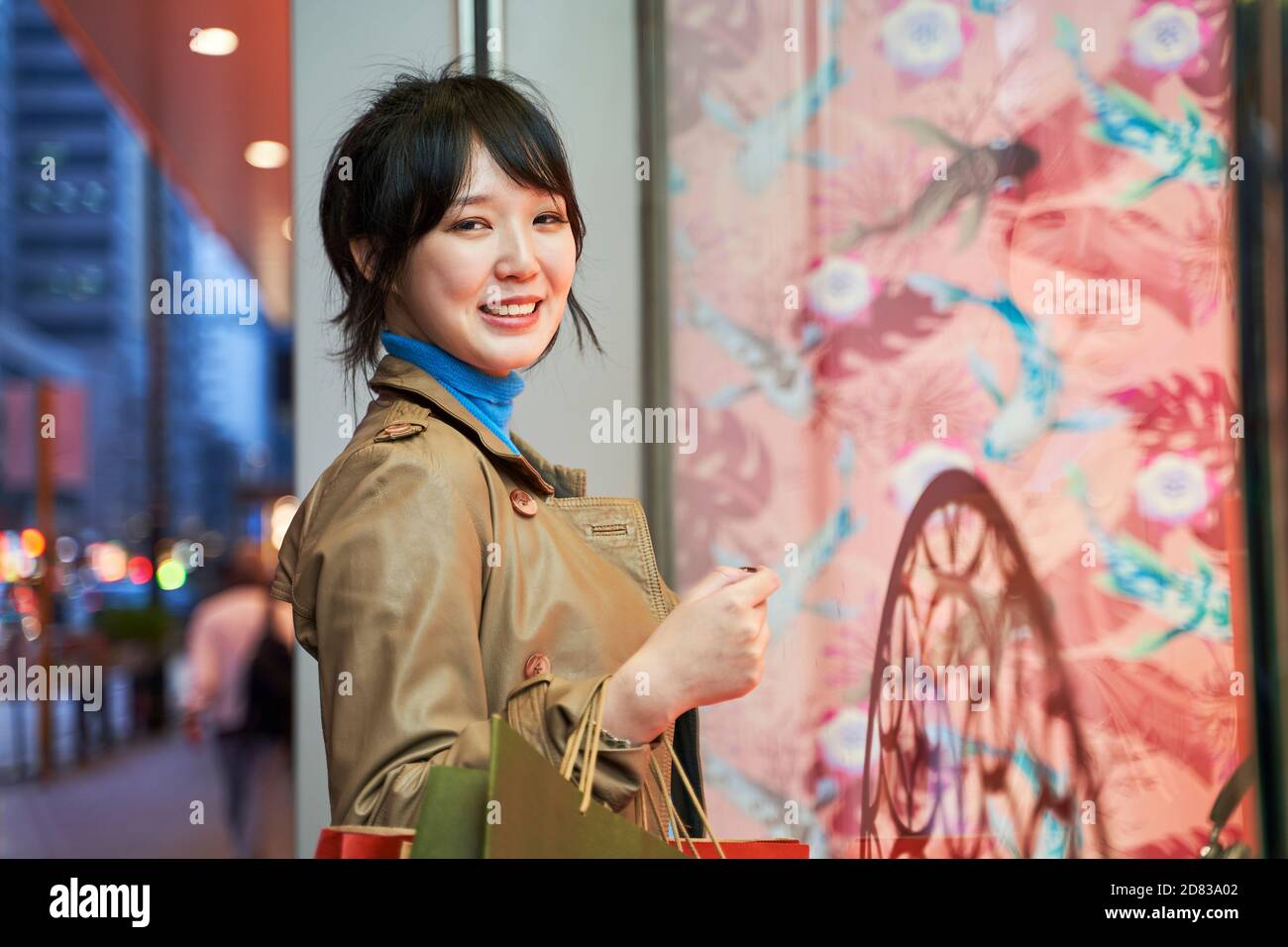 beautiful happy young asian woman shopper standing in front of shop window in modern city Stock Photo