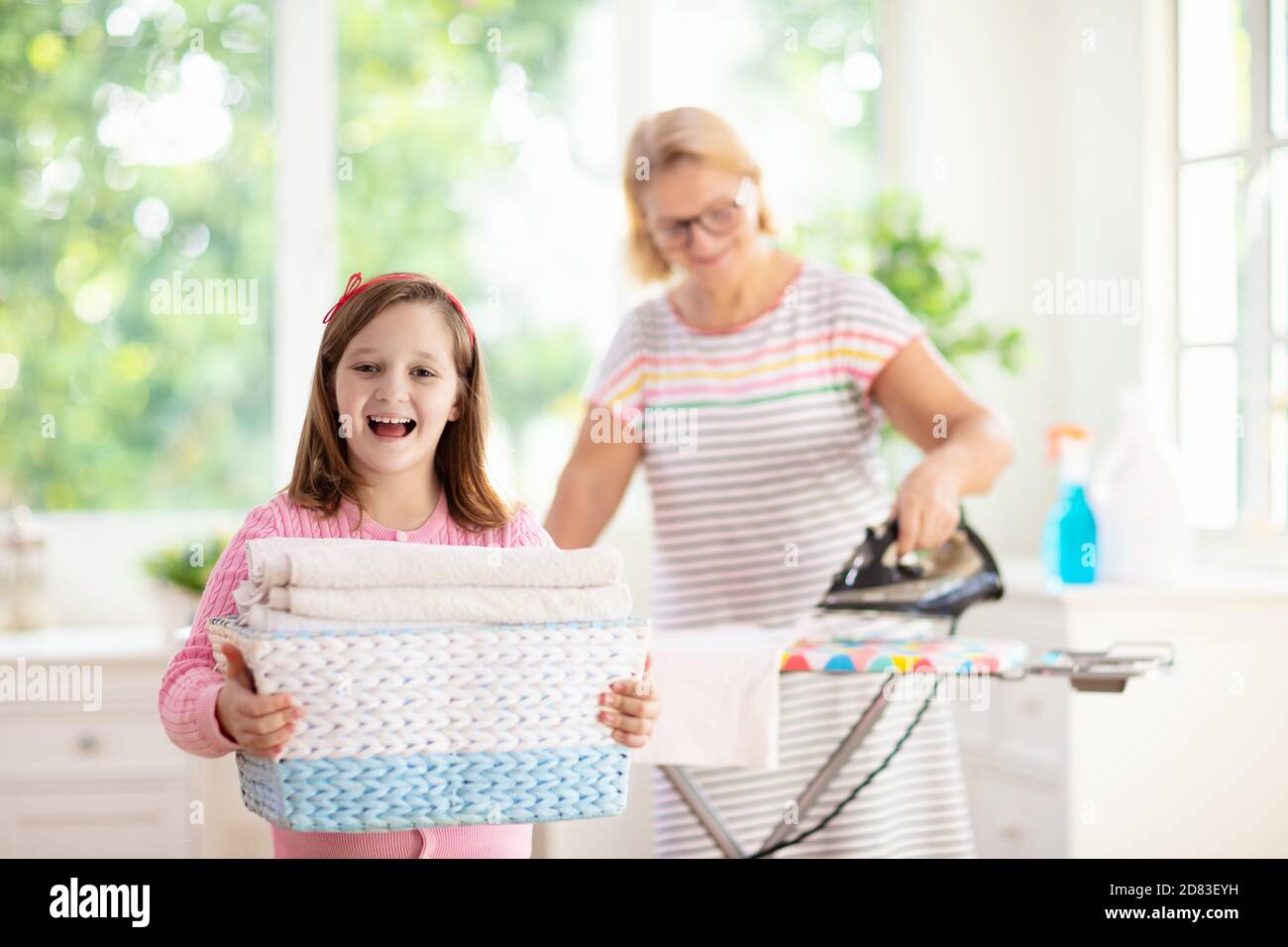 Woman and child ironing clothes. Mother and daughter folding clothes at iron board. Mom and kid cleaning house. Home chores. Stock Photo