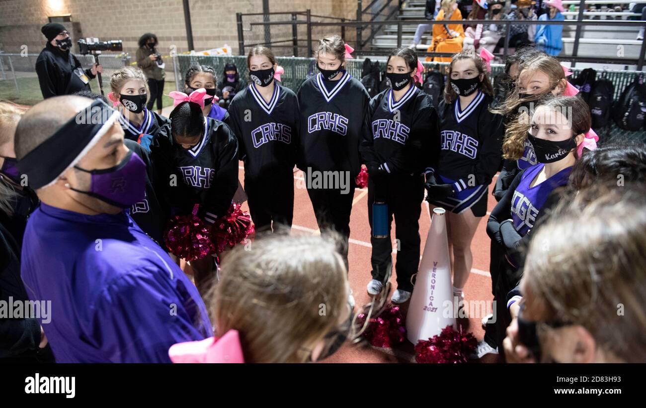 Masked-up Cedar Ridge High School cheerleaders rally around their coach before a District 25 6A high school football game on a chilly night at Dragon Stadium in Round Rock, Texas USA. Stock Photo