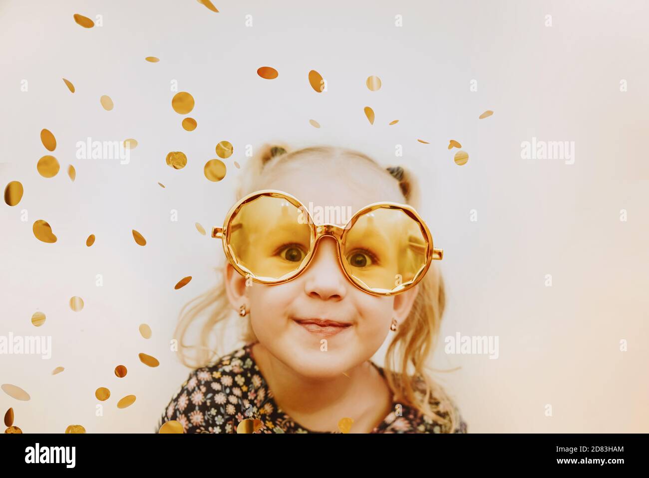 Little girl wearing gold masquerade glasses smiling and fooling around Stock Photo