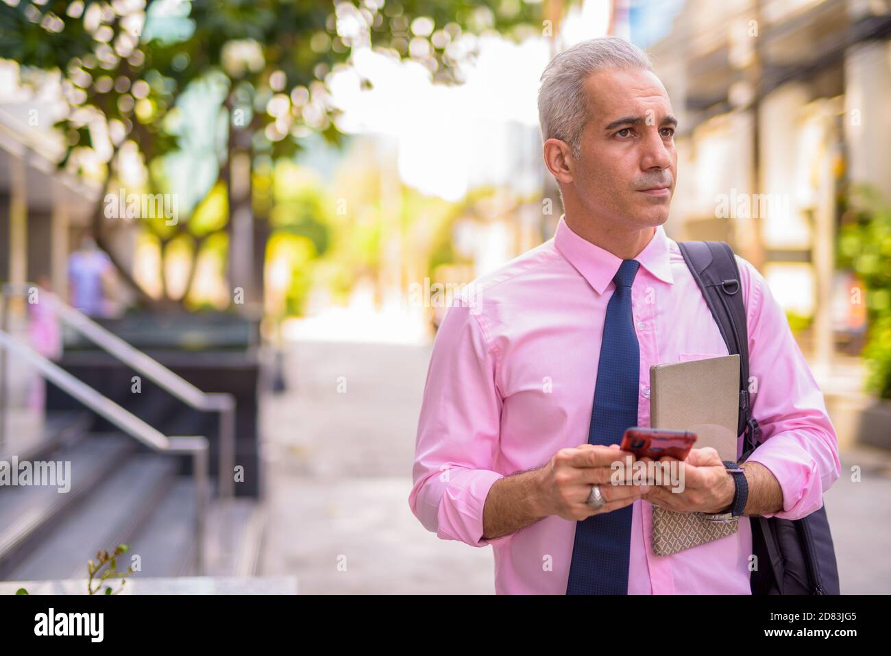 Handsome Persian businessman thinking while using phone in the city ...