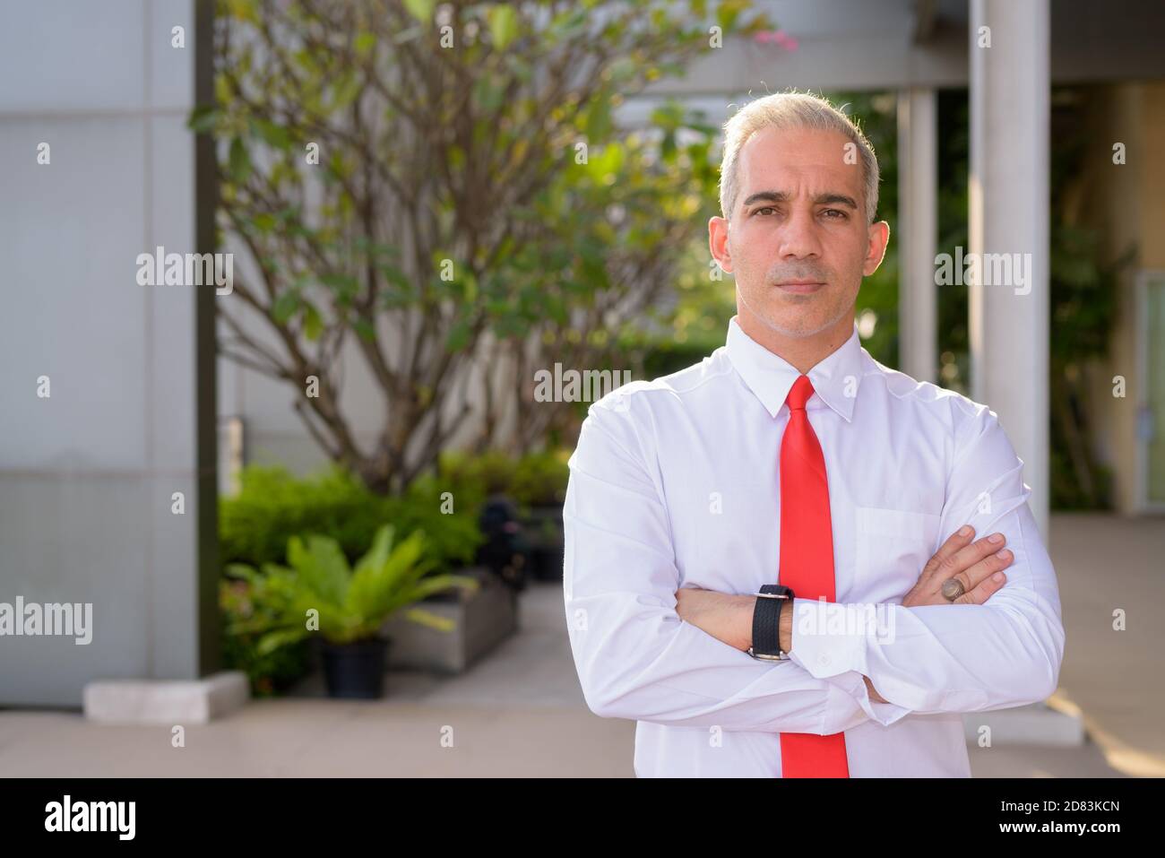 Handsome Persian businessman with arms crossed in the city streets ...