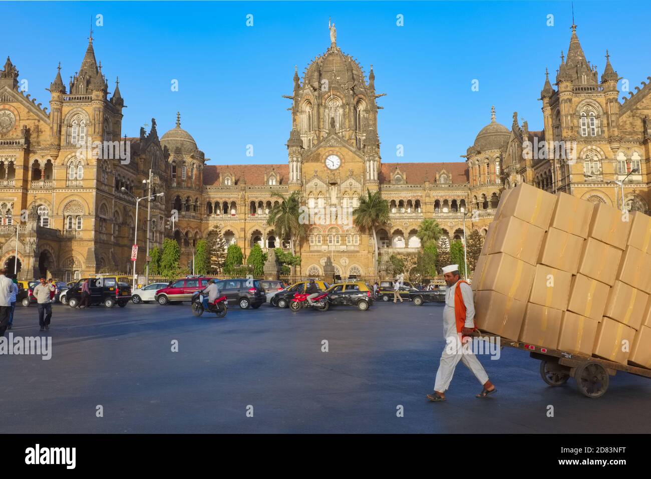 A handcart puller with fully loaded cart passes iconic Chhatrapati Shivaji Maharaj Terminus (CSMT), a UNESCO heritage site in Fort area, Mumbai, India Stock Photo