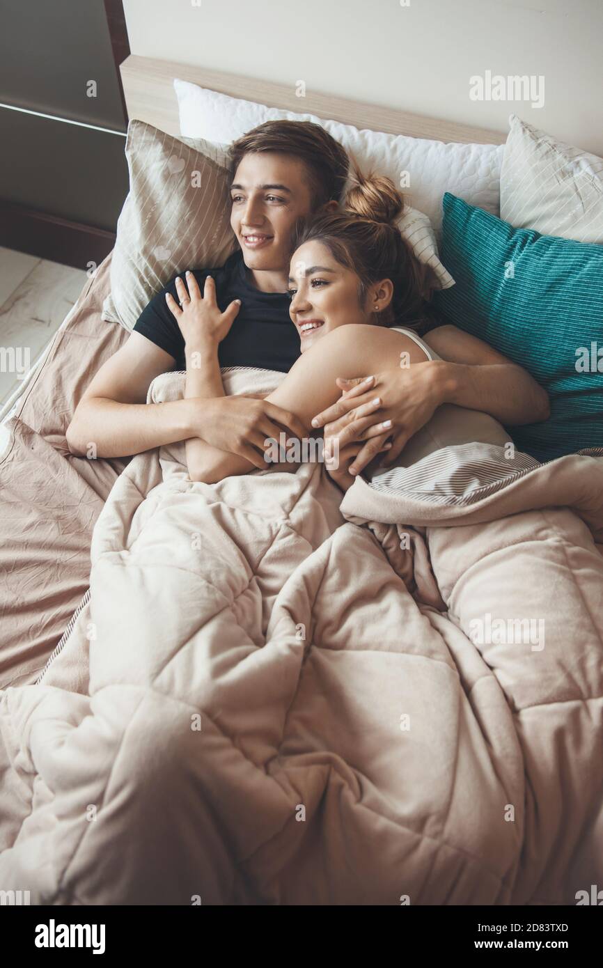 Upper view photo of a caucasian couple lying on bed embracing under a coverlet and smile in a morning Stock Photo