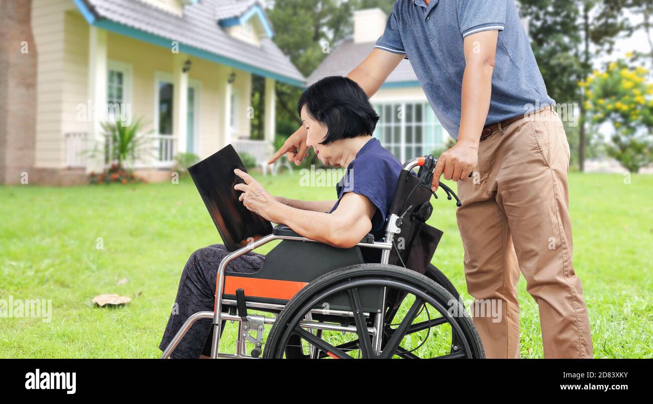 Asian elderly woman reading a book with her son take care in backyard Stock Photo