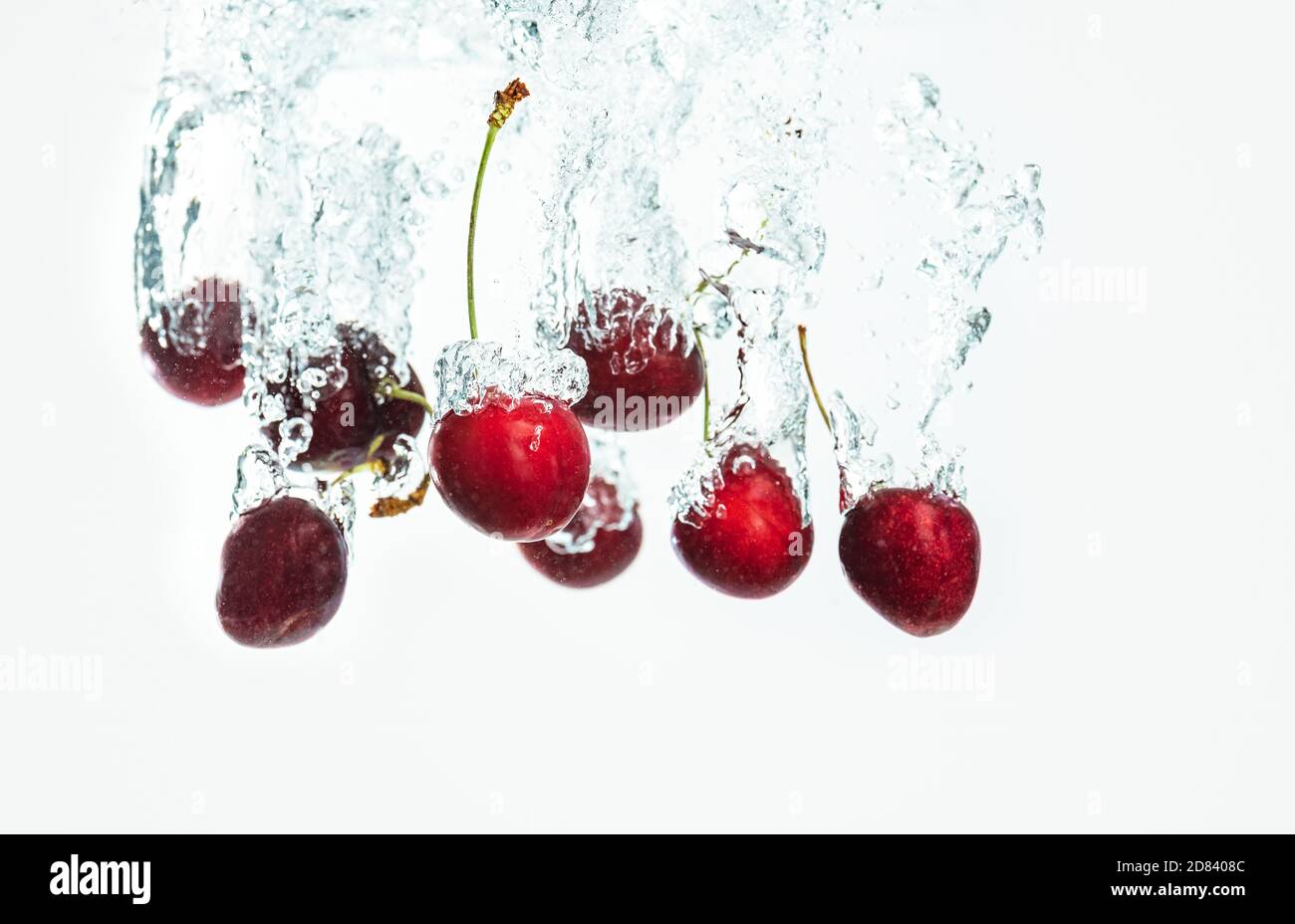 Red Cherries splashing into water against white background Stock Photo