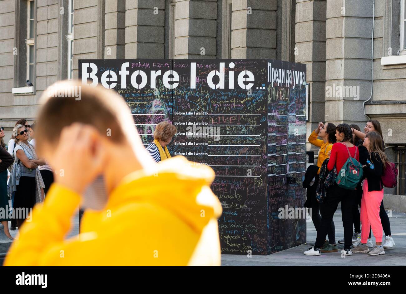 Passersby writing and reading messages on a blackboard or chalkboard wall for the Before I Die public interactive art project in Sofia Bulgaria Stock Photo