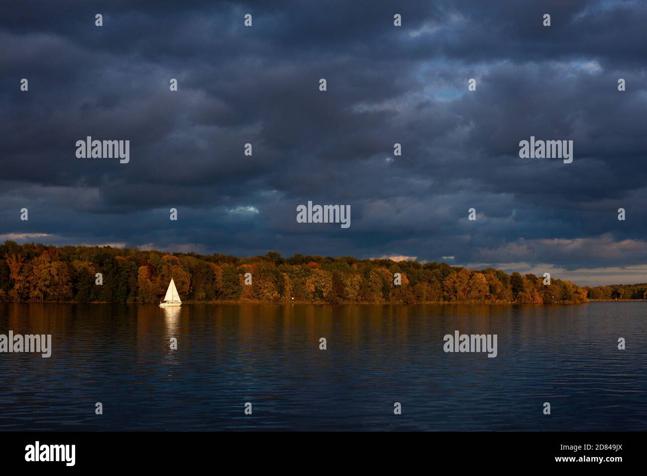 A sailboat catches the last light on an autumn evening, seen across the Jungfernsee from The Dairy in the New Garden in Potsdam, Germany Stock Photo