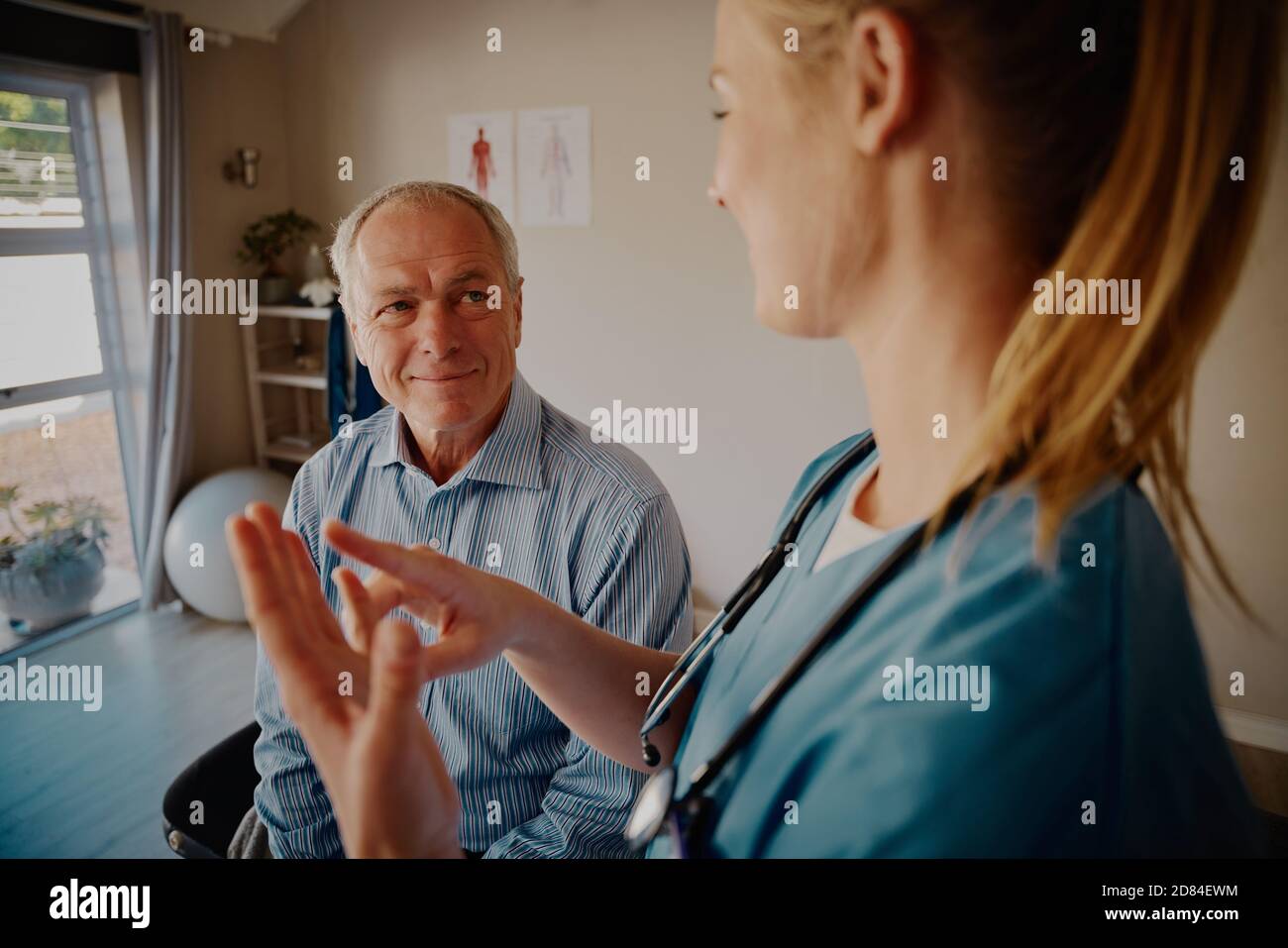 Smiling retired male patient listening to young female doctor while explaining about physiotherapy treatment Stock Photo