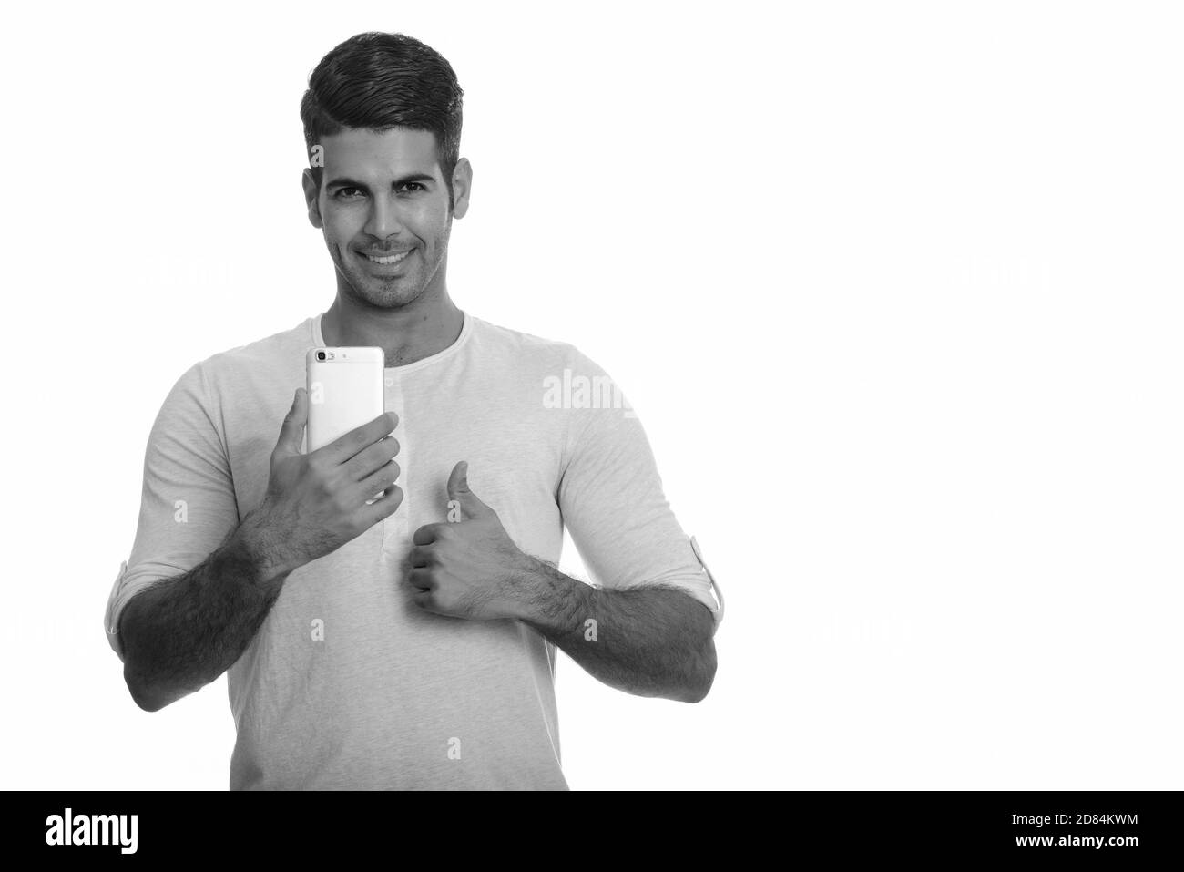 Young happy Persian man smiling while holding mobile phone and giving ...