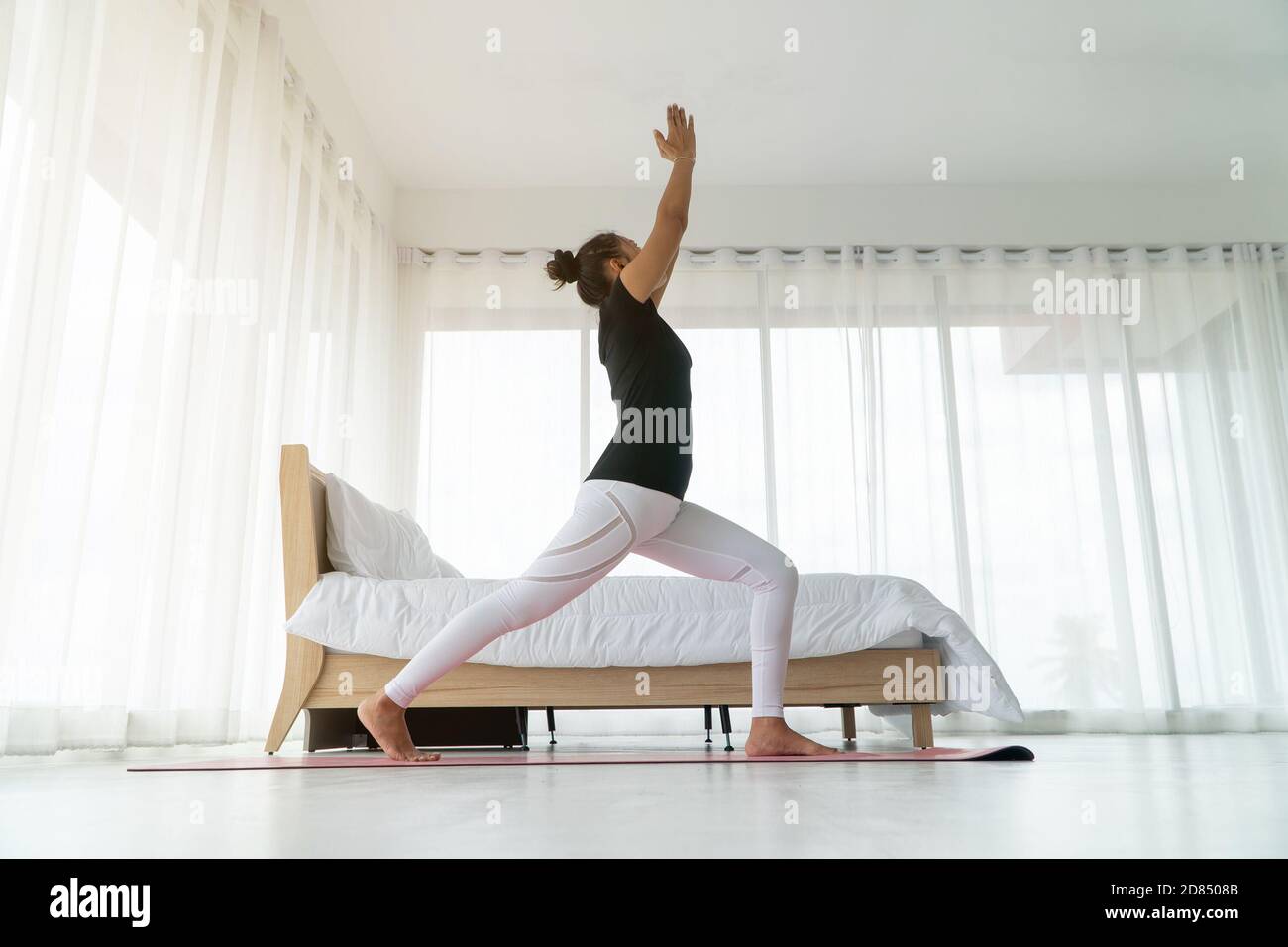 Middle aged women doing yoga in bedroom at the morning, adho mukha svanasana pose. Concept of exercise and relaxation in the morning. Stock Photo