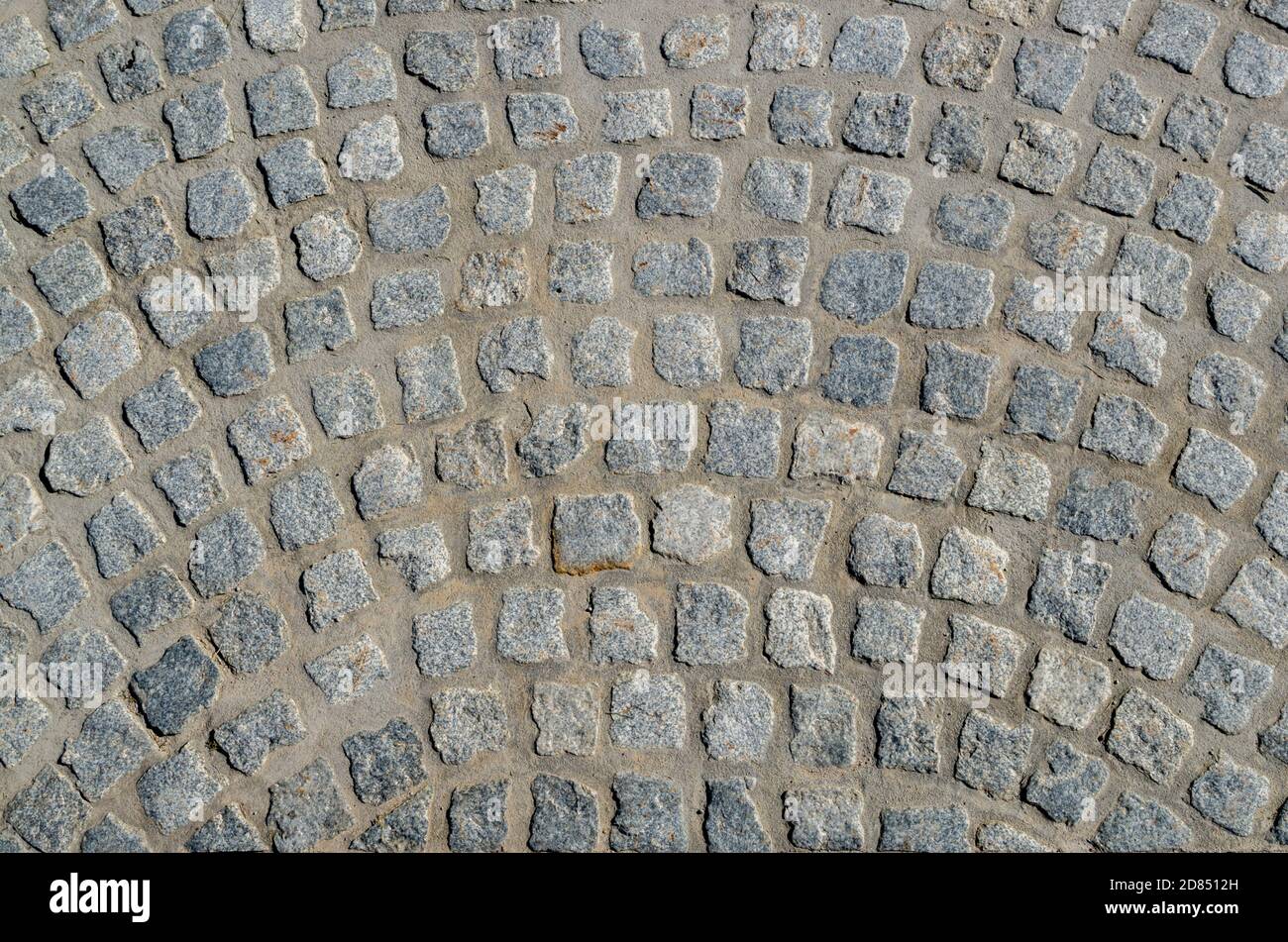 A fragment of pavement paved with rough square gray stone blocks with uneven edges in the form of semicircular arched streaks. Stock Photo