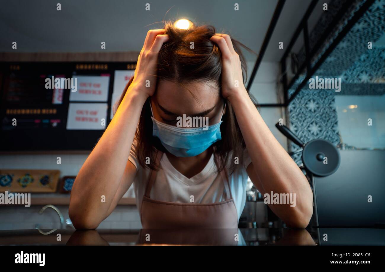 Asian woman coffee shop business owner Stressed and disappointed from The effects of the coronavirus pandemic resulting in business losses Stock Photo