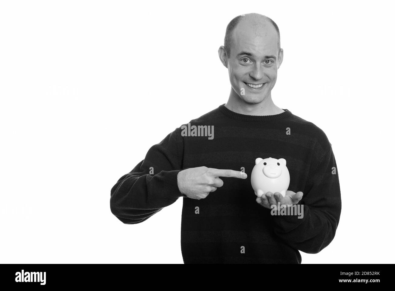 Happy bald Caucasian man smiling and holding piggy bank while pointing ...