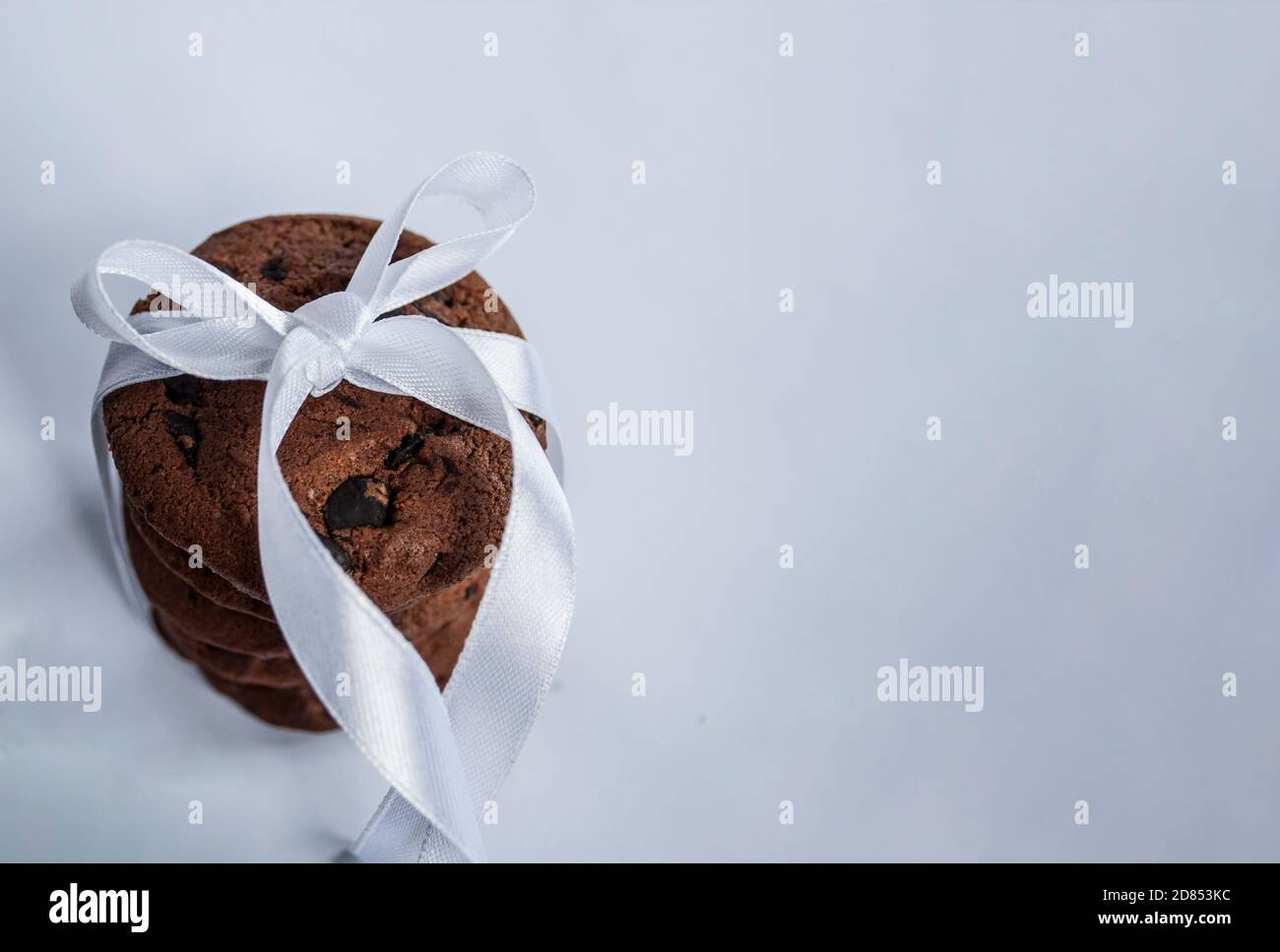 Stack of chocolate chip cookies with chocolate crumbs wrapped in white satin ribbon on a light background. Image with space for text. Selective focus Stock Photo