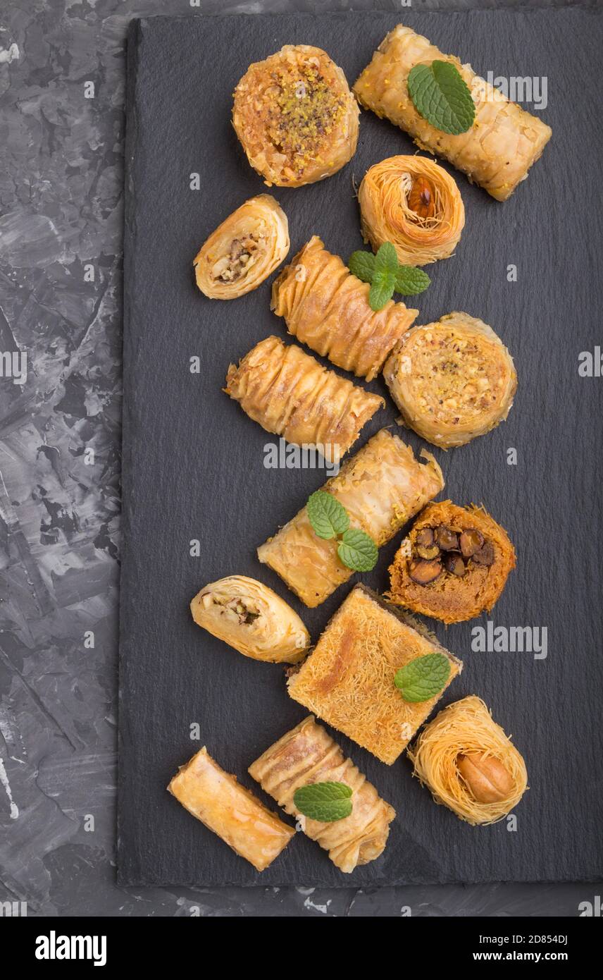 traditional arabic sweets (kunafa, baklava) on a black slate board on a black concrete background. top view, flat lay, close up. Stock Photo
