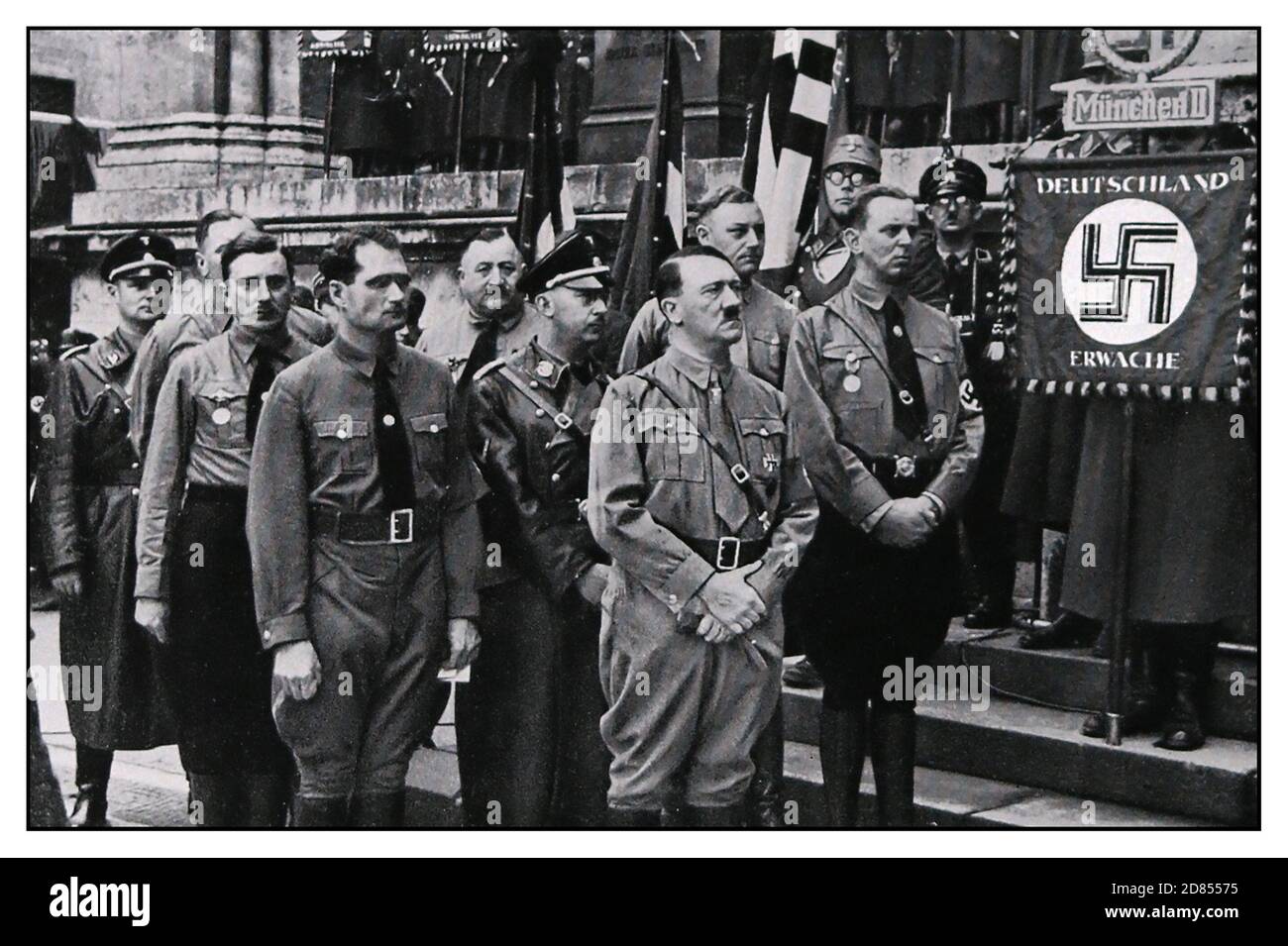 Vintage 1930's Nazi rally march in memory of Nazi victims of Beer Hall Putsch in Munich in 1920's. Adolf Hitler heads the group with Rudolf Hess to his right and Heinrich Himmler behind. Munich rally flag with 'Germany Awake' Stock Photo