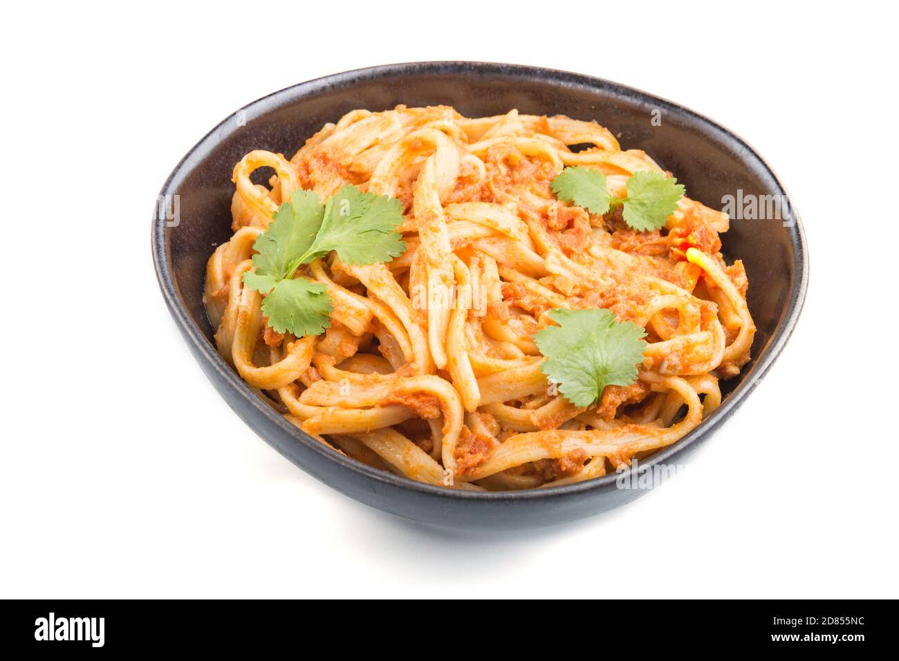 Semolina pasta with tomato pesto sauce, orange and herbs in bowl isolated on white background. Side view, close up. Stock Photo