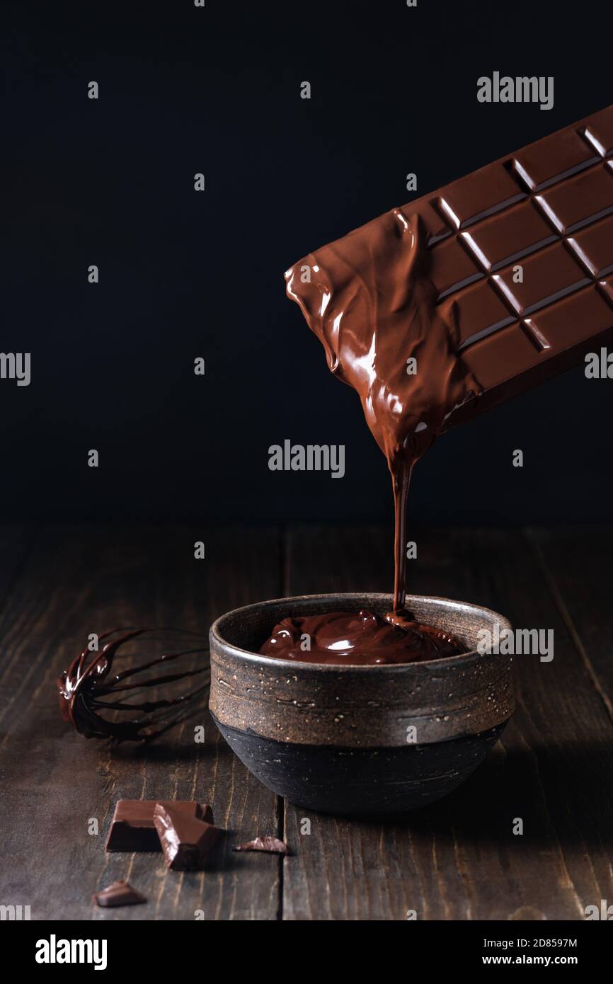 Dripping melted chocolate bar into ceramic bowl on dark background Stock Photo