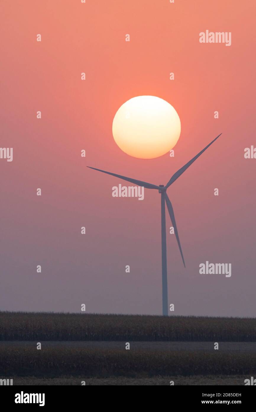 The morning sun rises over a farmland windmill. Stock Photo