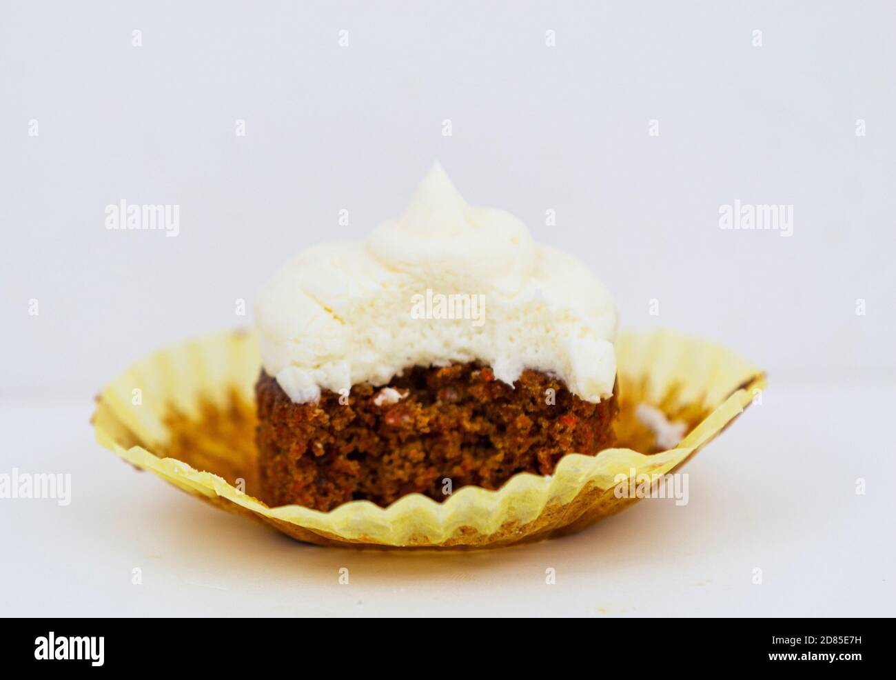 A carrot cake cupcake with cream cheese frosting and a white background has had a bite taken out of it. Stock Photo