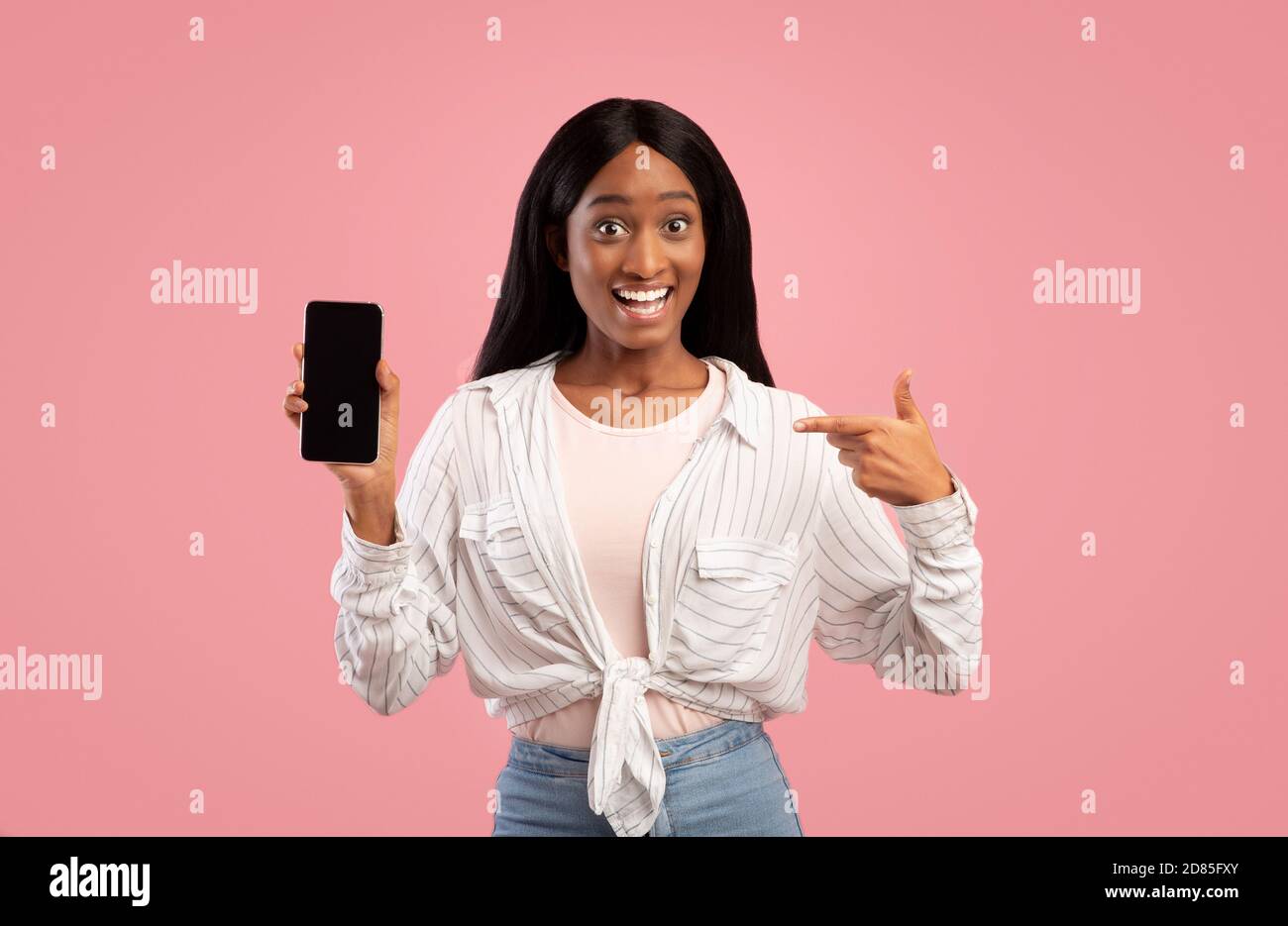 African American woman pointing at smartphone with empty screen on pink ...