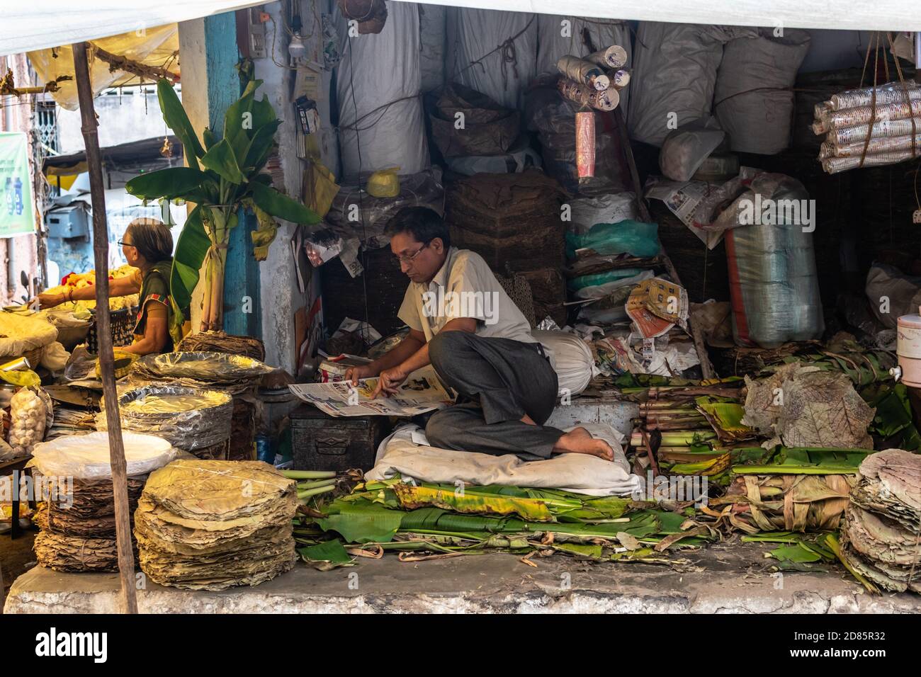 Nagpur, Maharashtra, India - March 2019: An Indian male vendor reading a newspaper inside his shop that sells banana leaves and plates. Stock Photo