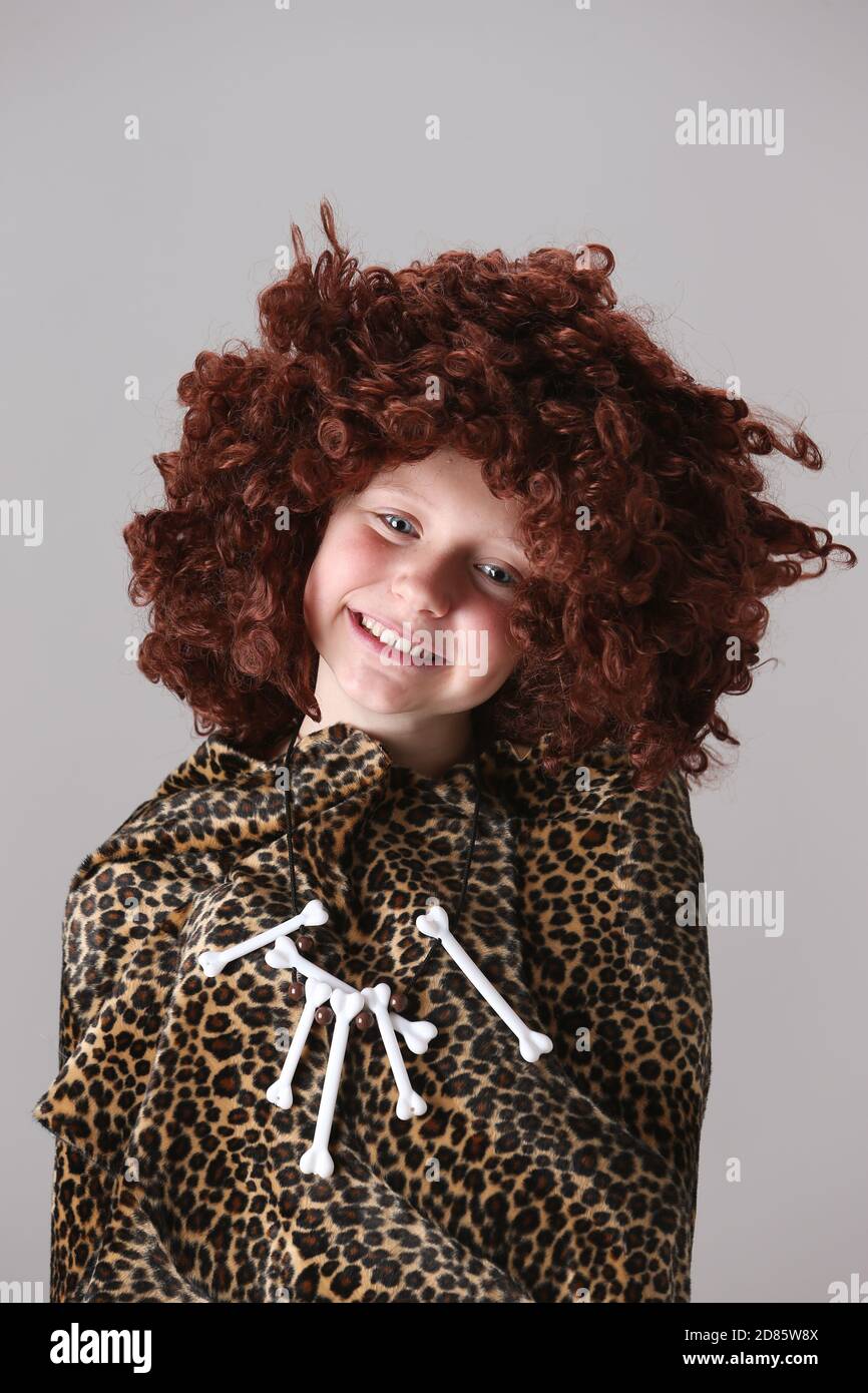 Smiling young girl in leopard skin cloak with 1960s,1970s style Afro wig wearing a necklace made of toy bones. Stock Photo
