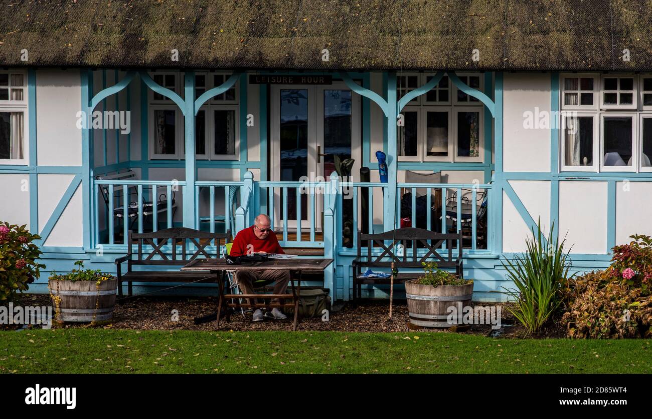 Man sitting on picnic bench outside thatched cottage, Wroxham, Norfolk, UK Stock Photo