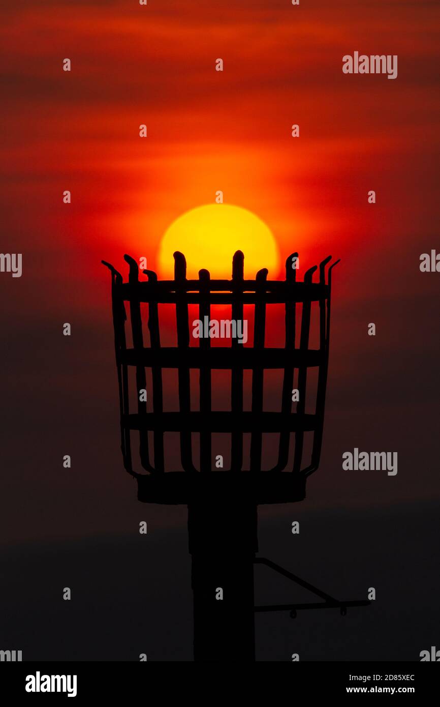 A vertical and creative colour photograph of a British iron fire beacon basket at sunrise with the basket catching the sun, Flamborough Head, Bridling Stock Photo
