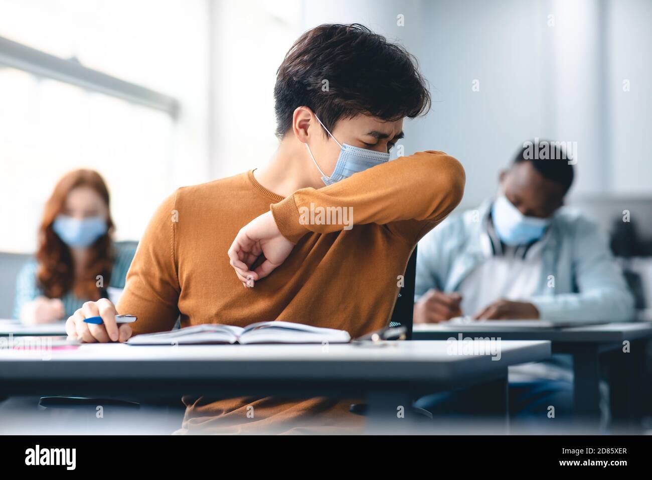 Asian male student couching in his elbow, sneezing in sleeve Stock Photo