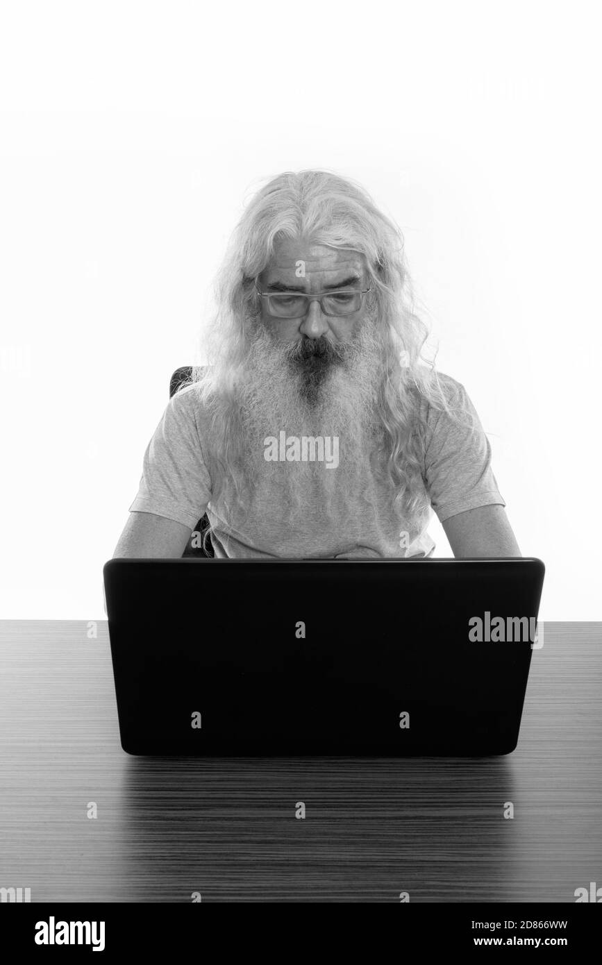 Senior bearded man wearing eyeglasses while using laptop on wooden table Stock Photo