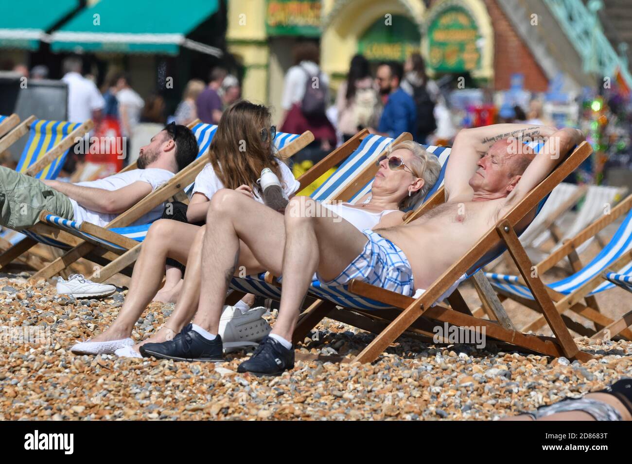A Caucasian couple sitting in deckchairs on a beach on a hot day in Spring in Brighton, East Sussex, England, UK. Stock Photo