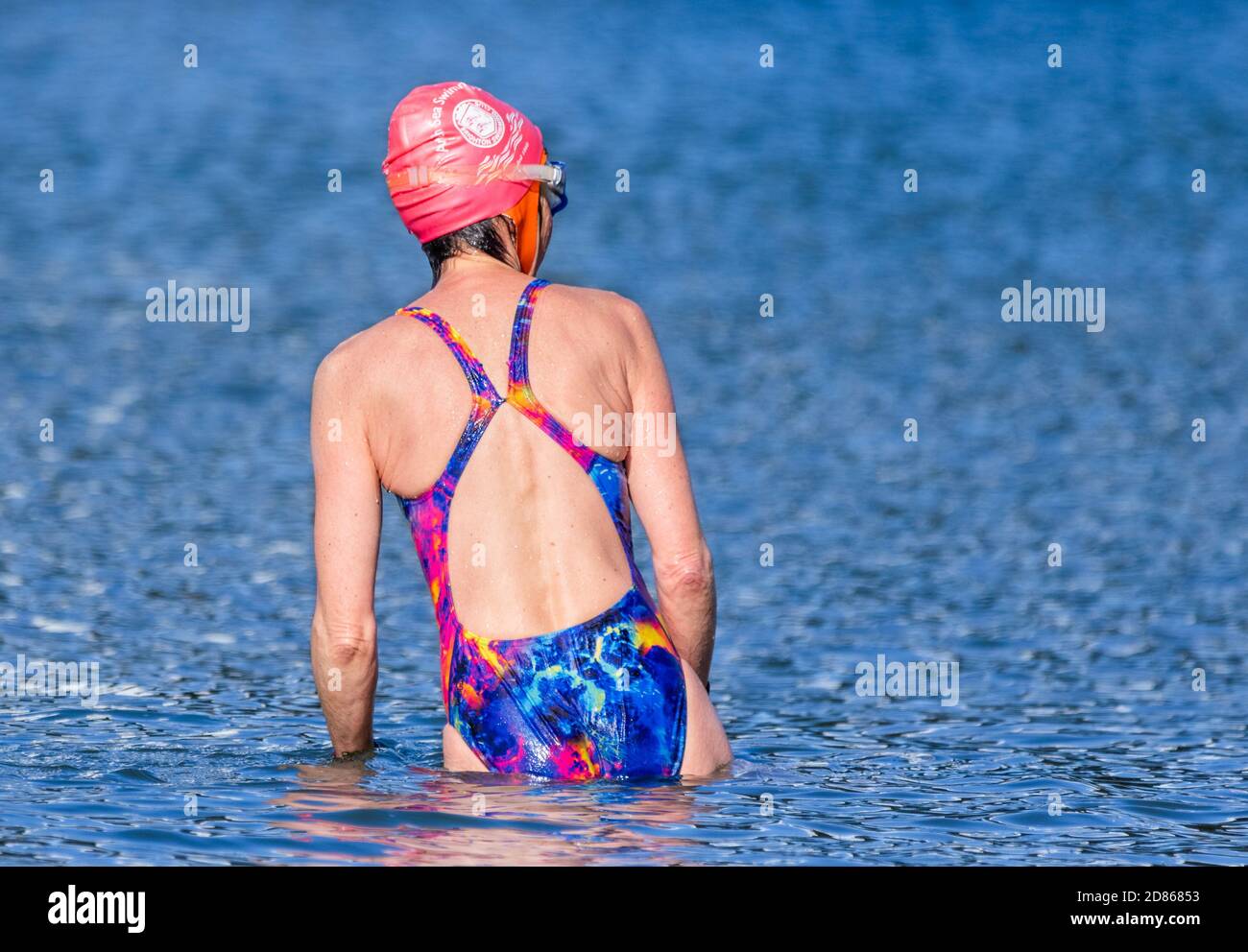 A woman wearing swimming cap and swimming costume about to swim in the sea in the UK. Stock Photo