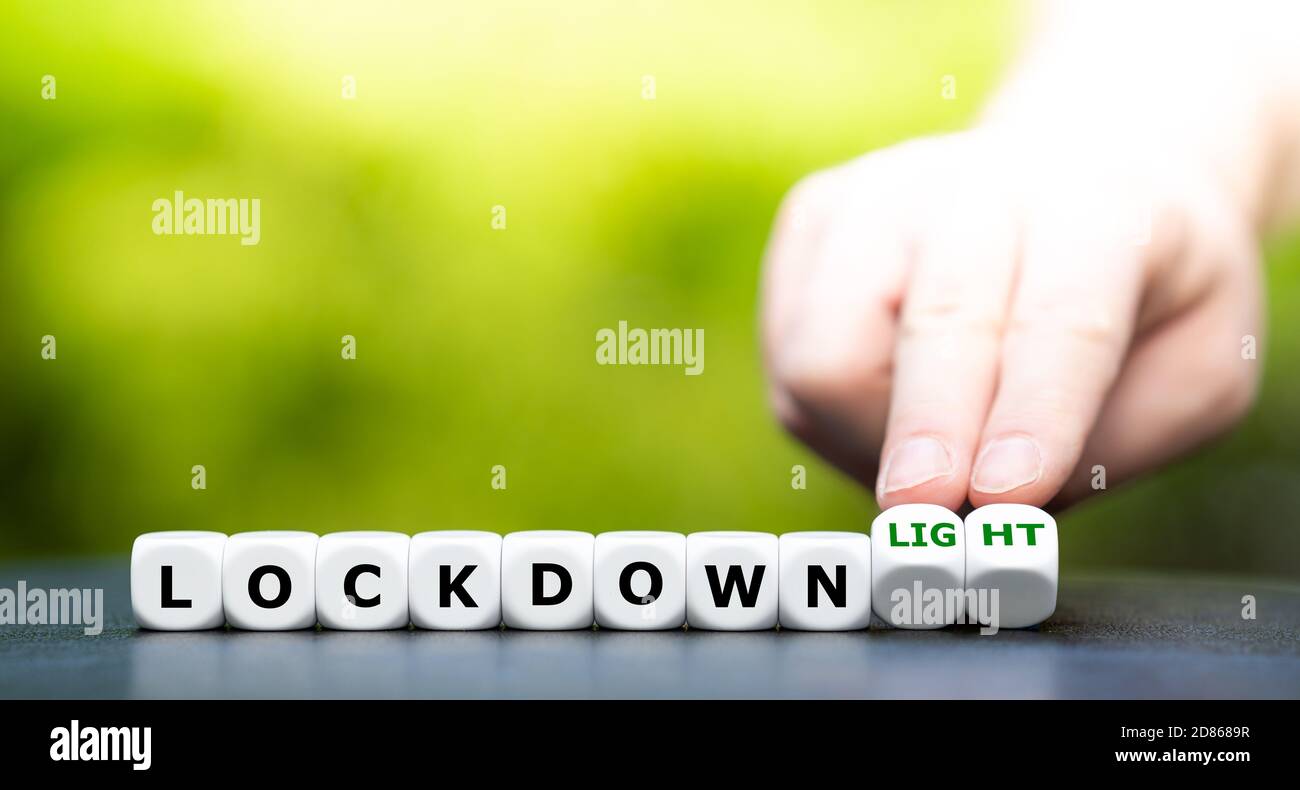 Symbol for a second lockdown. Hand turns dice and changes the expression 'lockdown' to 'lockdown light'. Stock Photo