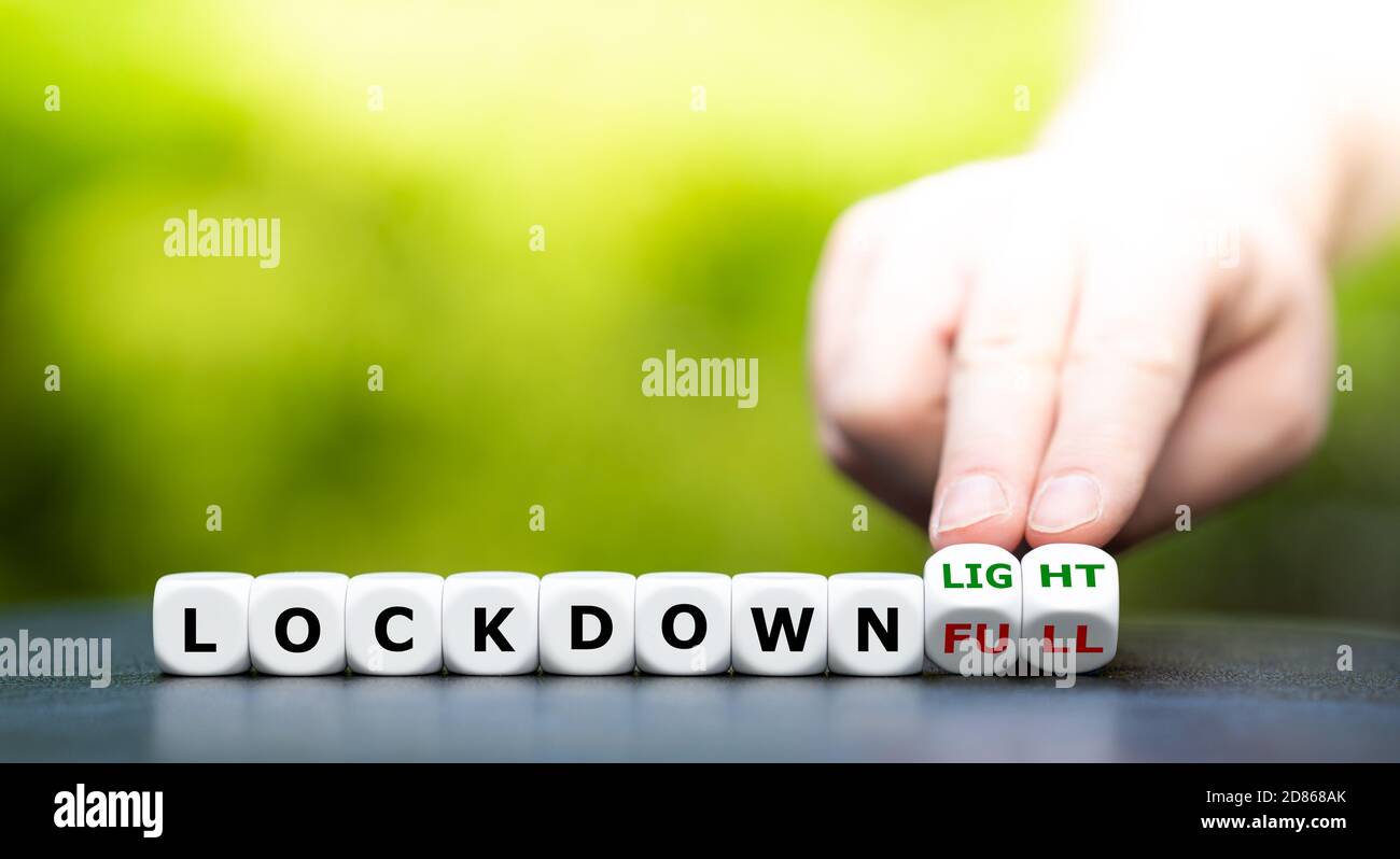 Symbol for a second lockdown. Hand turns dice and changes the expression 'lockdown full' to 'lockdown light'. Stock Photo
