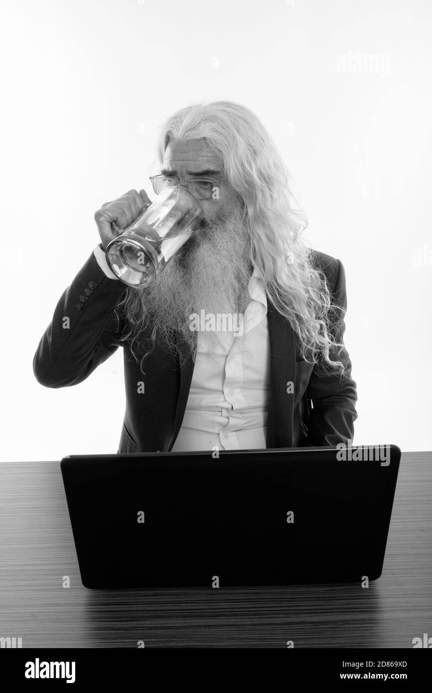 Studio shot of senior bearded businessman drinking glass of beer with laptop on wooden table Stock Photo
