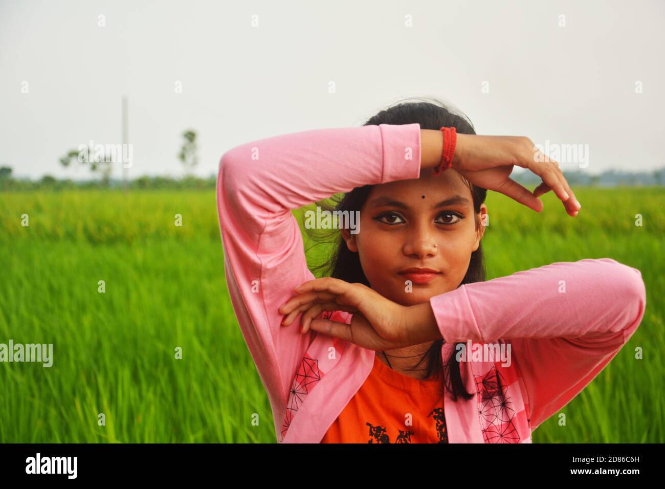 Close up of a teenager girl wearing pink color dress with hands on forehead and chin smiling on a paddy field, selective focusing Stock Photo