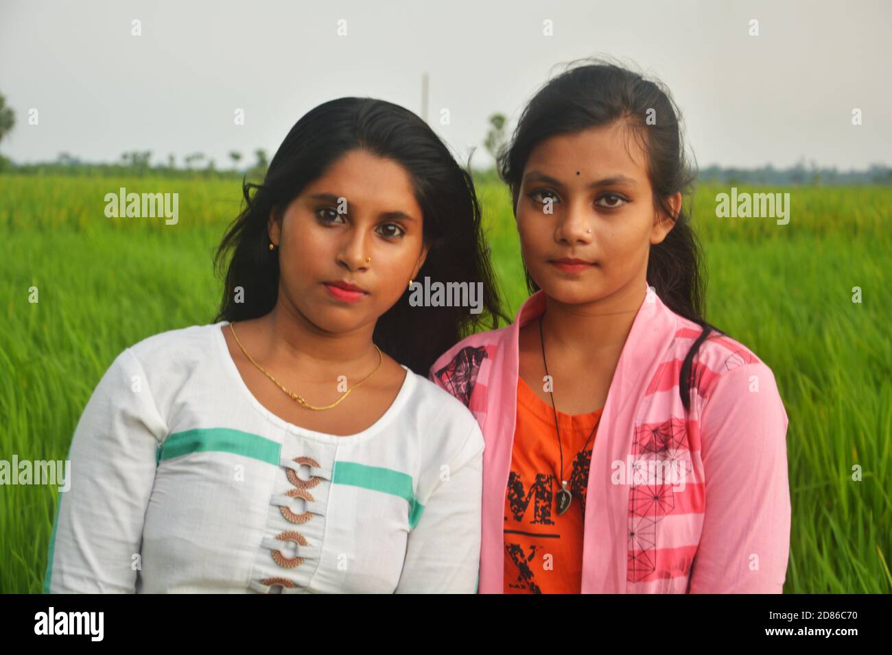 Close up of two teenager girls with long hairs wearing white and pink dresses with lipstick in a paddy field, selective focusing Stock Photo