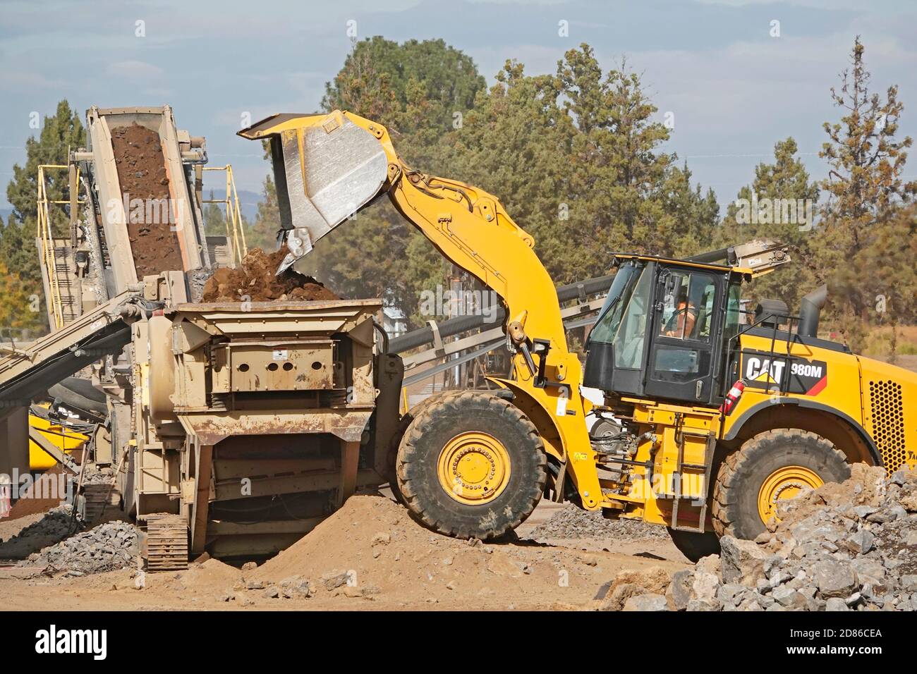 A large, earth moving tractor on a construction site in Bend, Oregon, moves boulders into a rock crusher to make gravel. The construction site is for Stock Photo