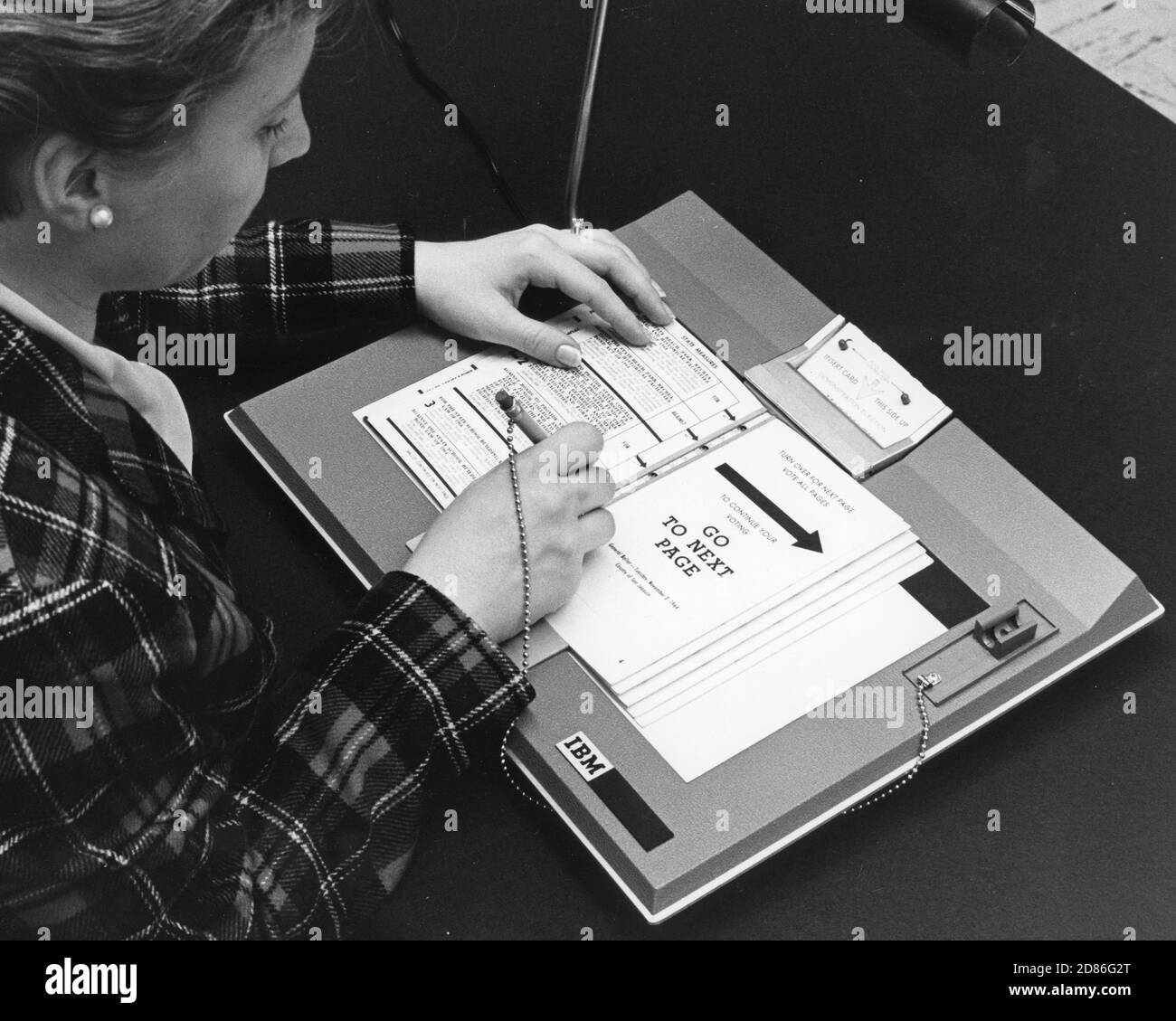 Woman demonstrates a simple voting machine made by IBM in which the voter casts ballot by punching holes in a card which drops into a ballot box. At the end of the day, cards are run through an electronic machine that totals the votes, 1966. (Photo by International Business Machines/United States Information Agency/RBM Vintage Images) Stock Photo