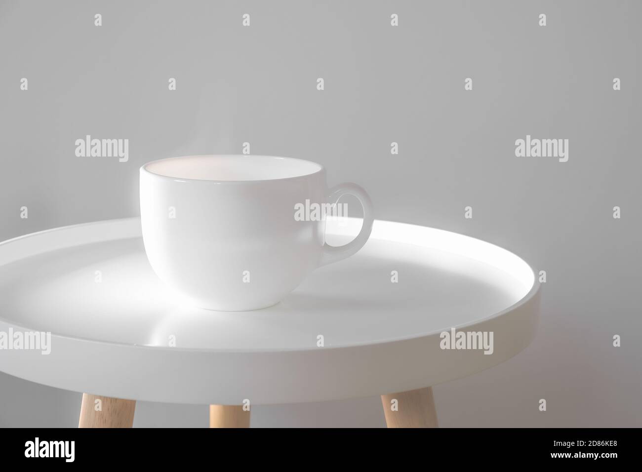 Mug with hot drink on a white coffee table indoors. Scandinavian interior style, minimalism in house, tranquil living concept Stock Photo