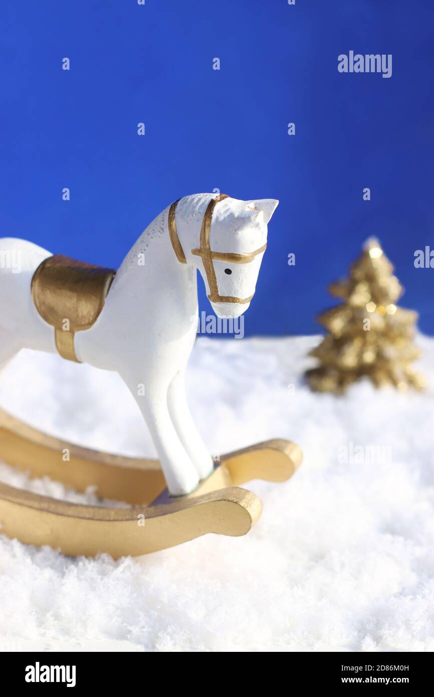 blue and white christmas greeting card with a rocking horse and a gold colored tree in the back Stock Photo