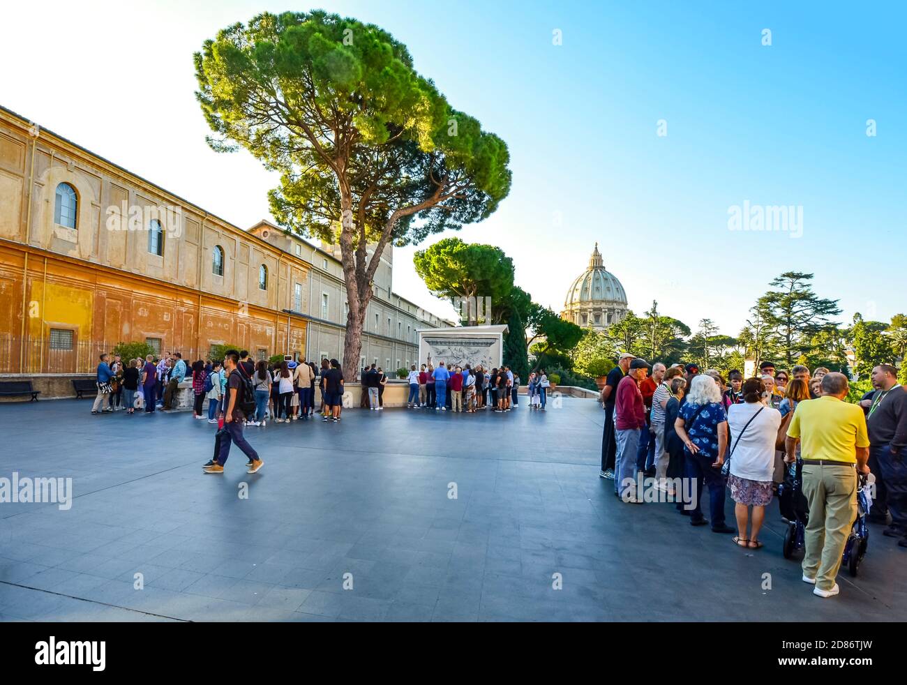 Tour groups gather in separate areas on top of the Vatican museum with the dome of St Peter's Cathedral Basilica in view in the distance. Stock Photo