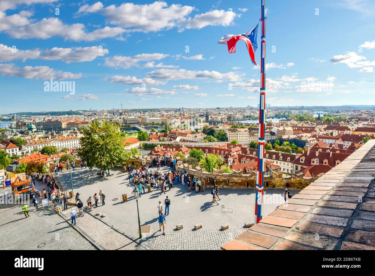 City view and skyline from atop the Prague Castle Complex with tourists below and a Czech flag flying on a flagpole. Stock Photo
