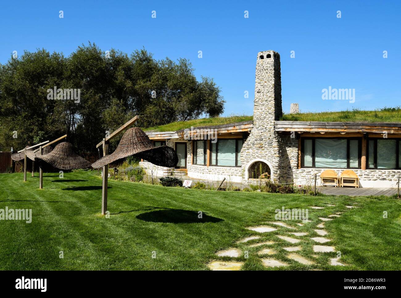 Old stone restaurant as the hobbit's house. Umbrellas made of woven branches photographed on a sunny day with blue sky. Stock Photo