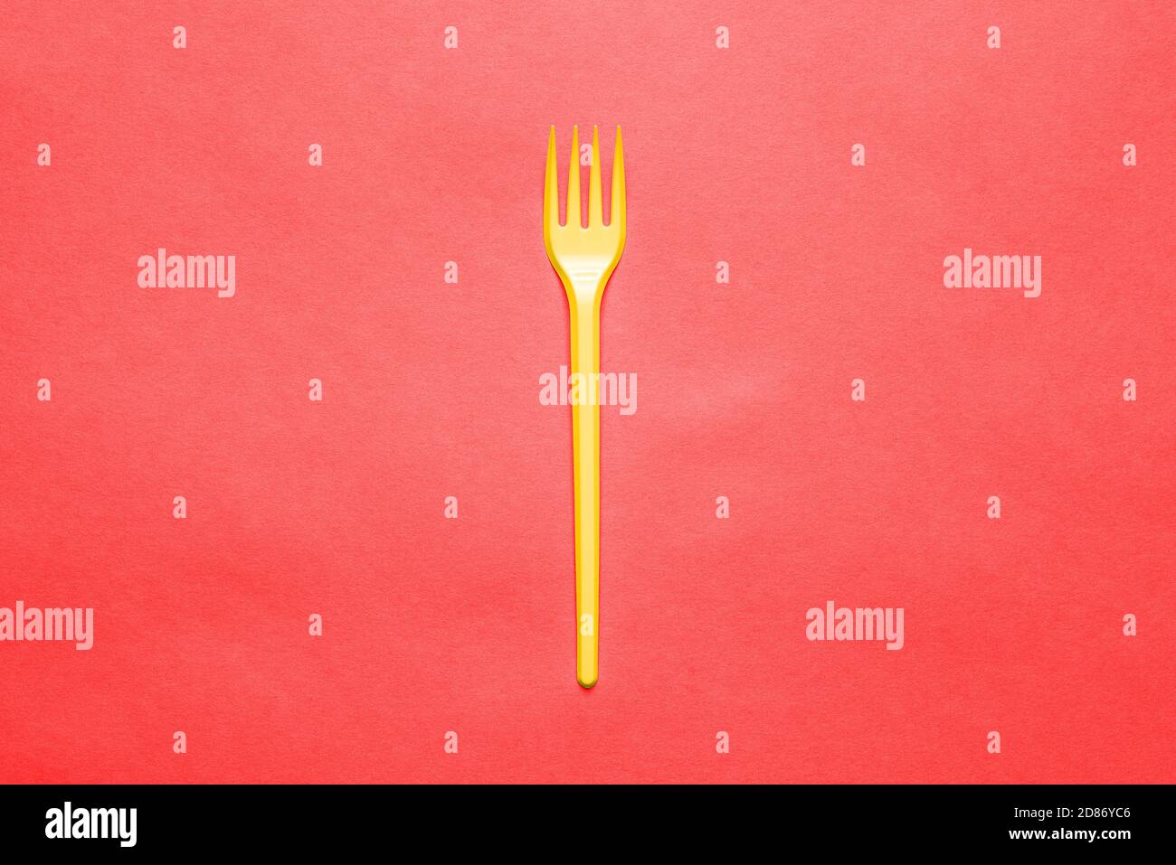 Yellow plastic fork on a red background. Disposable Cutlery for eating. Dinnerware. Creative minimal style Stock Photo