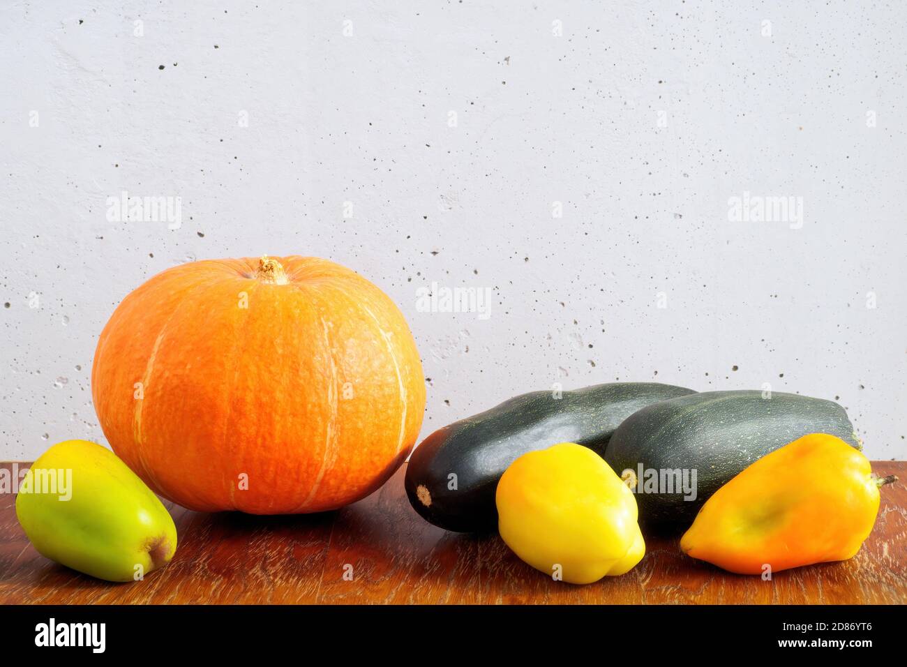 Orange pumpkin, dark green zucchini and bell peppers on wooden table on gray concrete wall background. Copy space Stock Photo
