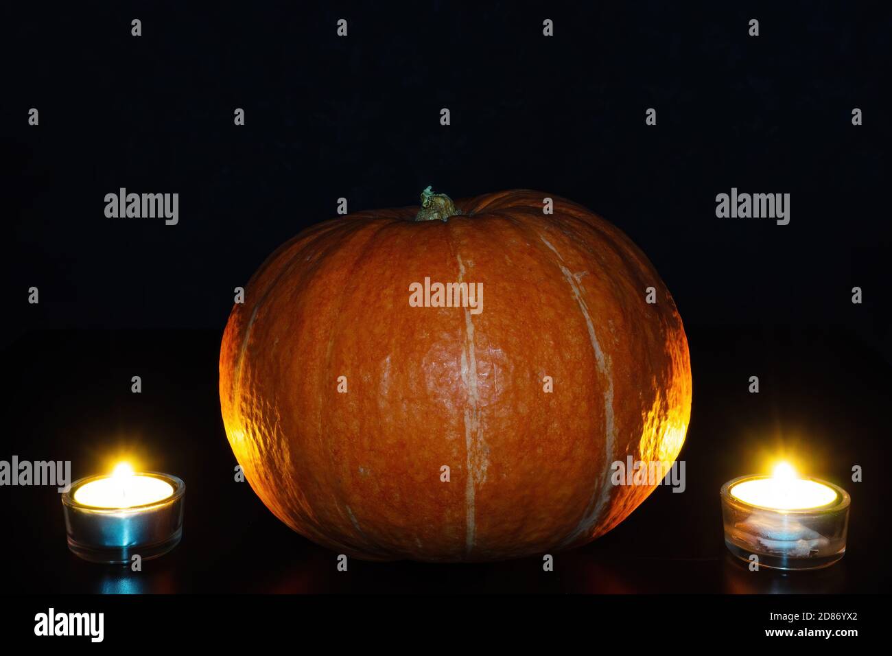 Orange pumpkin and two lighted tea candles on black background. Halloween concept Stock Photo
